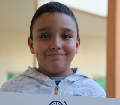 Image of a boy in Morocco holding up a sign saying migration means voyager